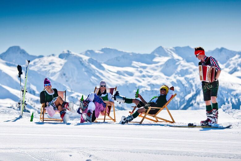 Skiers relaxing in deckchairs on a sunny Alpine piste with an accordion player in traditional dress